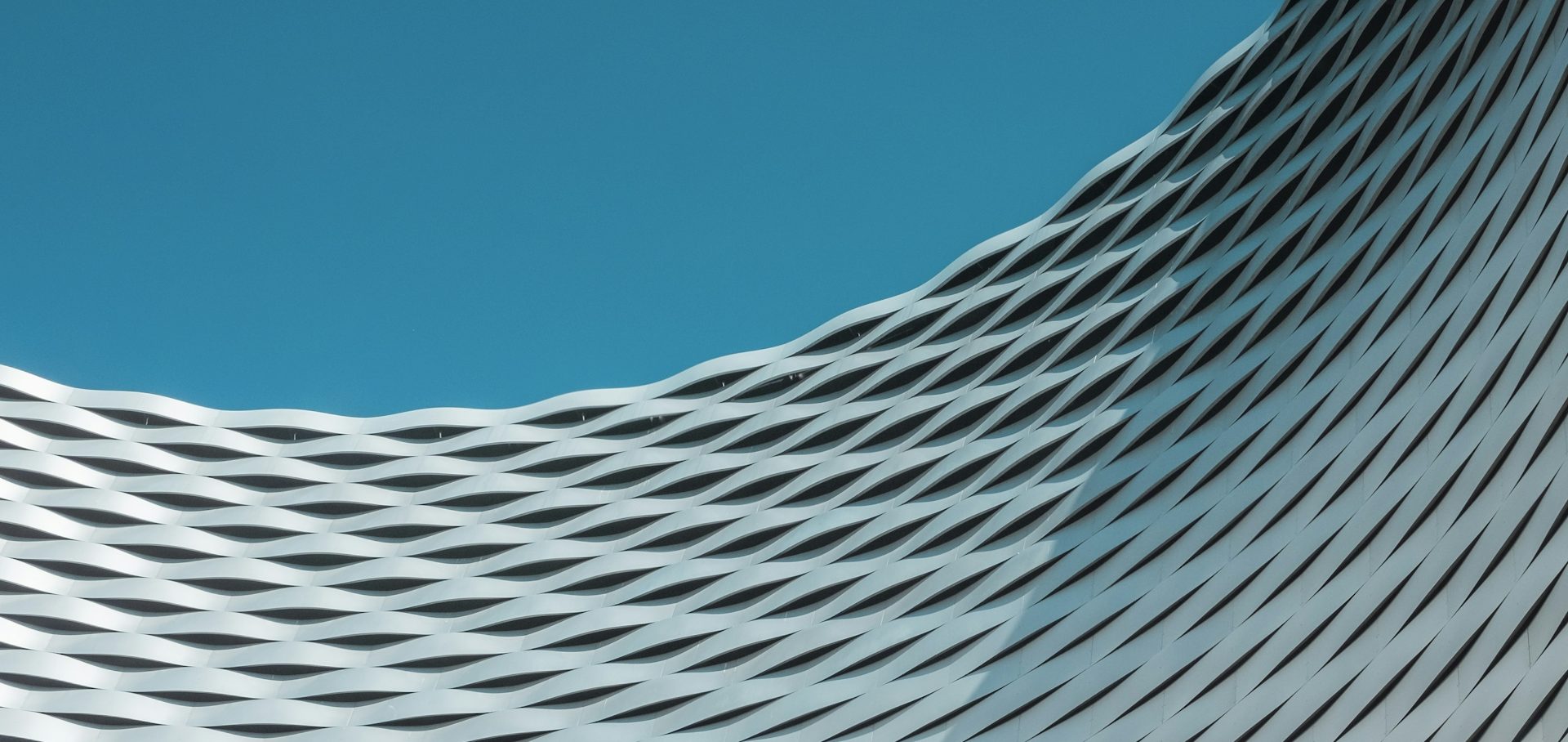 Schwungvolle, gewebte Metallstruktur vor einem blauen Himmel.